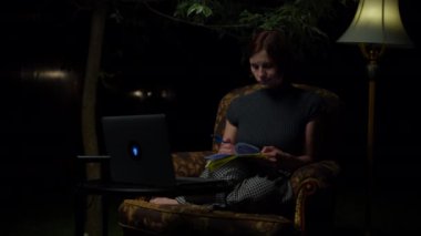 30 'lu yaşlardaki genç bir kadın gece geç saatlere kadar online çalışmaktan rahat koltukta oturmaktan ve arka bahçesinde lamba taşımaktan yoruldu. Yetişkin öğrenci dizüstü bilgisayarını atıyor ve kapatıyor..