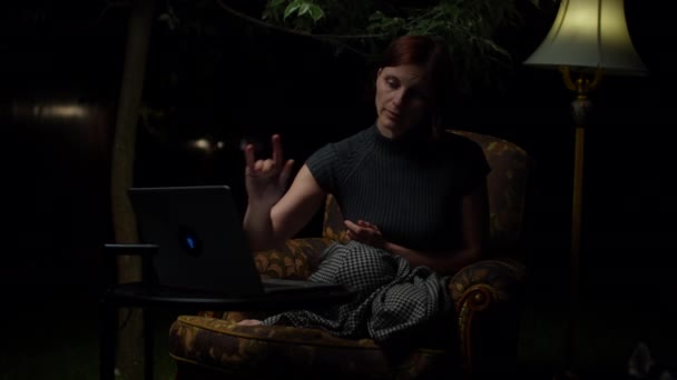 Eine junge Frau in den 30er Jahren, die es leid ist, spät in der Nacht online zu reden, sitzt in einem gemütlichen Sessel mit Stehlampe im Hinterhof. Frau schließt Laptop und legt Kopf auf Knie. — Stockvideo
