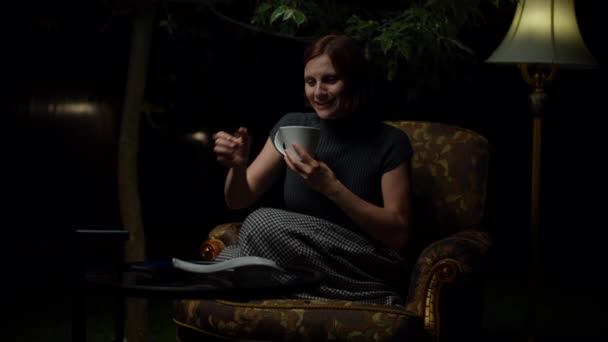 Genç mutlu kadın gece geç saatlerde cep telefonuna cevap veriyor. Arka bahçesinde lamba olan rahat koltukta tek başına oturuyor. Kadın cep telefonu aramasına sevindi.. — Stok video