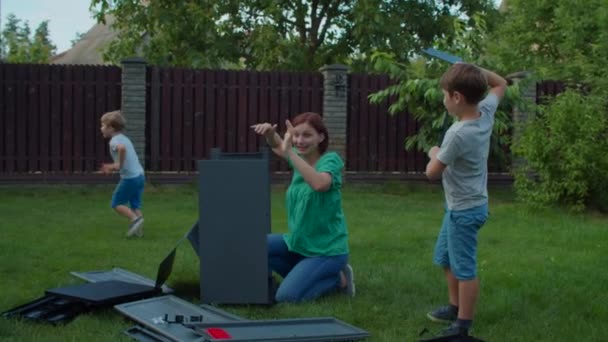 Familj till ung ensamstående mor och två barn monterar möbler med instruktion i trädgården på solig dag. Glad familjesemester utomhus. Slow motion, steadicam skott. — Stockvideo