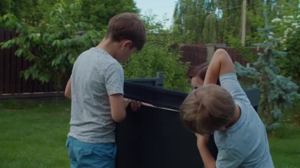 Twee broers helpen jonge alleenstaande moeder om meubels te monteren met instructie in de achtertuin op zonnige dag. Gelukkige familie activiteiten buiten. Langzame beweging, standvastig schot.. — Stockvideo