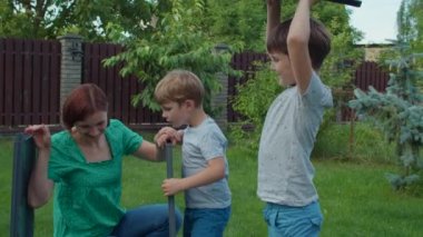 Genç bekar anne ve iki çocuklu aile güneşli bir günde arka bahçede mobilya montajı yapıyor. Mutlu aile hafta sonu aktiviteleri. Yavaş çekim, sabit çekim..