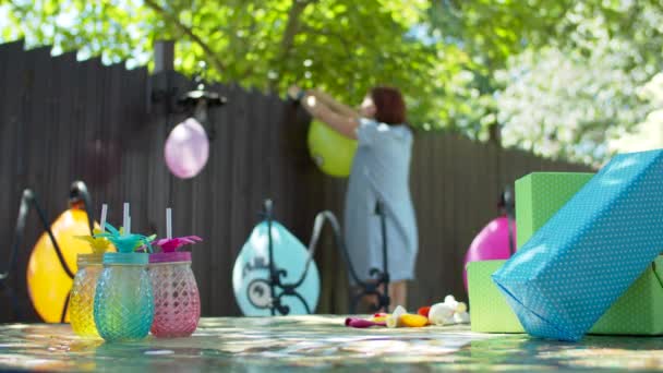 色風船で子供の誕生日パーティーのための裏庭を飾る若い30の母親。パーティーの装飾のために気球を吹く女性. — ストック動画