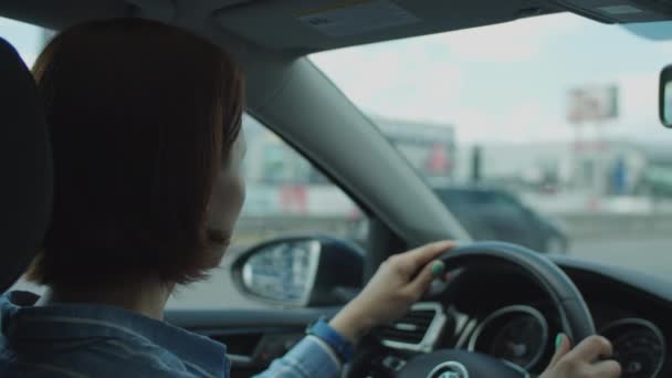 Молода 30-річна жінка водить машину в місті. Вид збоку жінки водій тримає кермо . — стокове відео