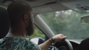 Şehirde araba süren sakallı genç bir adam. Direksiyonda el ele tutuşan sürücünün yan görünümü.