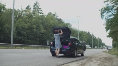 30 'lu yaşlarda, kırmızı üçgen takan genç bir kadın otoyolda kırık bir arabanın yanında dur işareti olarak duruyor. Yolda araba kazası..