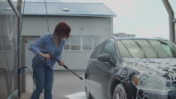 Jeune femme trentenaire laver sa voiture familiale en libre-service lavage de voiture. Femme lave l'automobile avec la mousse et l'eau à l'extérieur. — Video