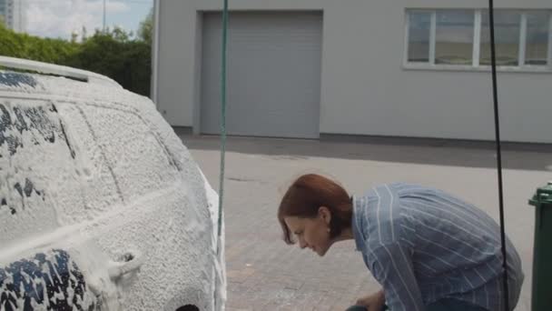 Mujer joven de 30 años lavando su coche familiar en auto servicio de lavado de coches. La hembra lava el automóvil con espuma y agua afuera . — Vídeos de Stock