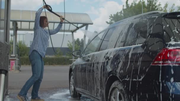 Jeune femme trentenaire laver sa voiture familiale en libre-service lavage de voiture. Femme lave l'automobile avec la mousse et l'eau à l'extérieur. — Video