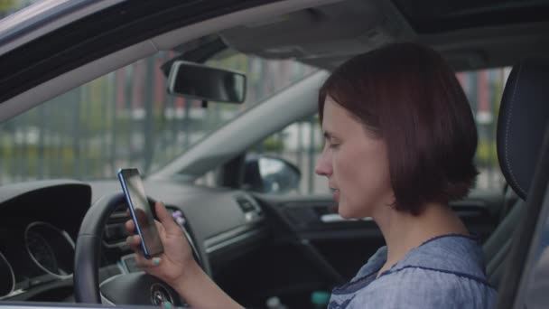30 років жінка, використовуючи мобільний телефон, сидить у машині. Жінка-водій тримає камеру в руках і серфінг онлайн . — стокове відео