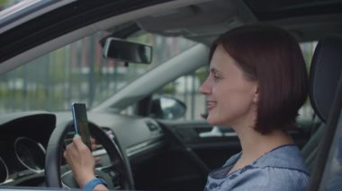 Arabada oturan 30 'lu yaşlarda bir kadın cep telefonuyla konuşuyor. Kadın sürücü hücreyi elinde tutuyor ve internette konuşuyor..