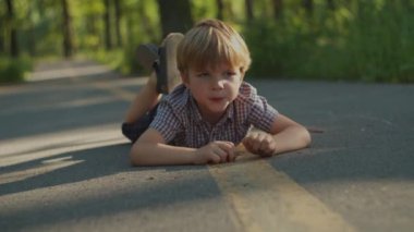 Düşünceli sarışın anaokulu çocuğu şehir parkında yolda yatıyor. Kaygısız çocuk dışarıda yerde yatıyor..