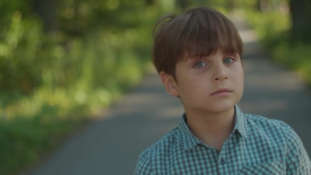 Дитячий портрет надворі. Шкільний хлопчик у сорочці, що стоїть у міському парку в літній час. Дитячий портрет . — стокове відео