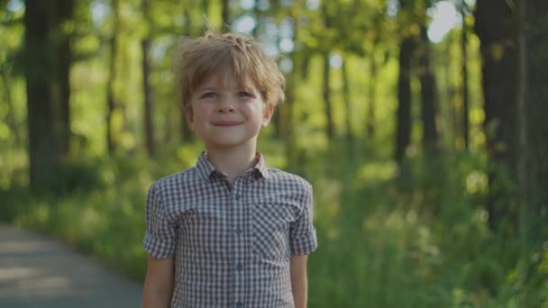 Školák v košili se usmívá, dívá se do kamery, stojí v městském parku v létě. Dětský portrét venku. — Stock video
