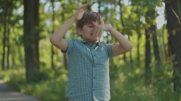 Niño de escuela con autismo haciendo movimientos divertidos con su pelo, de pie en el parque de la ciudad en verano. Retrato autista de niño afuera. — Vídeo de stock