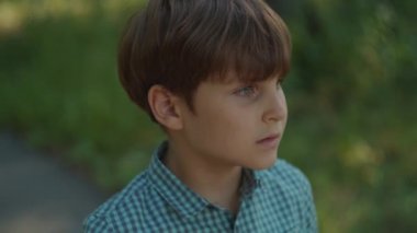 Otistik çocuk portresi dışarıda. Okul çocuğu yazın şehir parkında dikiliyor. Düşünceli çocuk portresi.