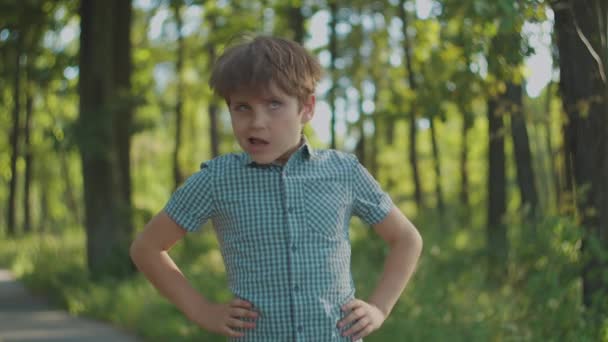 Школьник с аутизмом делает забавные движения головой, стоя в городском парке летом. Детский портрет снаружи. — стоковое видео