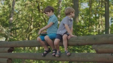 Dışarıda bir aleti olan iki çocuk. Büyük kardeş tablet bilgisayar kullanıyor, küçük kardeş dargın..