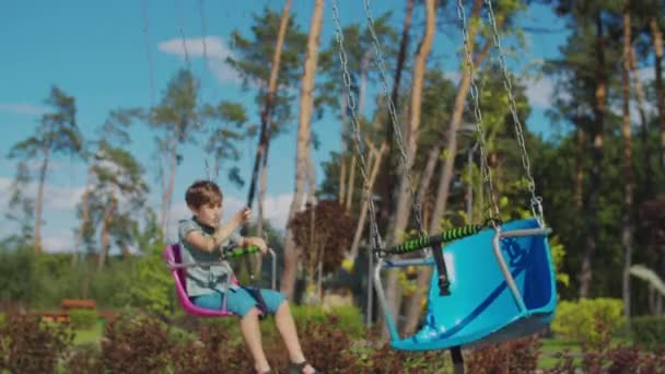 Dos niños montando carrusel de chairoavión de color en la feria. Los hermanos se divierten solos en el parque. Distancia social durante la cuarentena. — Vídeo de stock