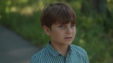 Okul çocuğu yazın şehir parkında dikilirken sessizlik işareti gösteriyor. Ağzı işaret parmağı olan bir çocuk. Otistik çocuk sessiz olmak istiyor.. 