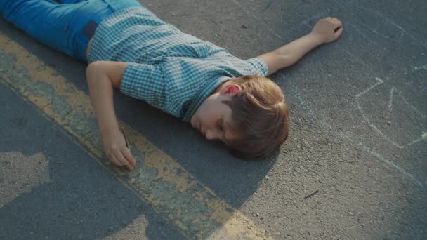 公園の小道に寝そべっている少年。地面に木の棒で遊ぶ自閉症の少年. — ストック動画