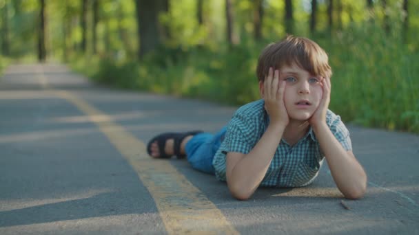 Anak sekolah terbaring di jalur taman. Autistik anak berpikir di tanah. — Stok Video
