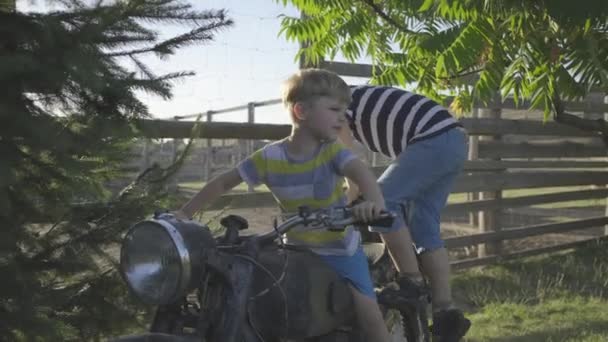 Rodzeństwo bawi się starym motocyklem na zewnątrz. Dzieci udają, że jeżdżą na motocyklu. Zabytkowy pojazd w parku. — Wideo stockowe