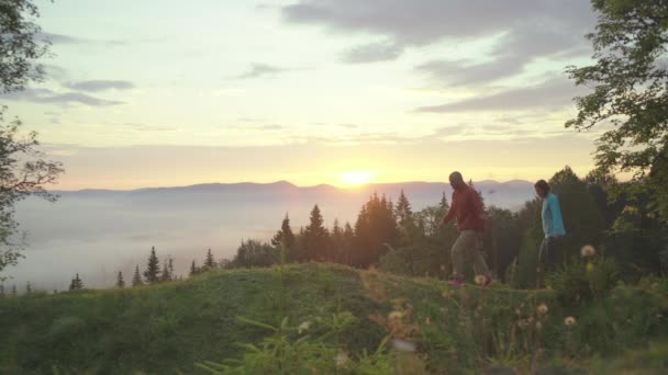 Homme et femme marchent sur la colline et saluent le lever du soleil dans les montagnes. Couple heureux jouit de beaux paysages tôt le matin. — Video