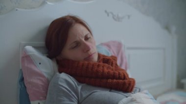 Hasta genç kadın yatakta yatıyor. Boyun öksürüğünde sıcak atkısı olan kadın. Peçeteli el göründü ve kadın burnunu sildi. Virüs Hastalığı. 