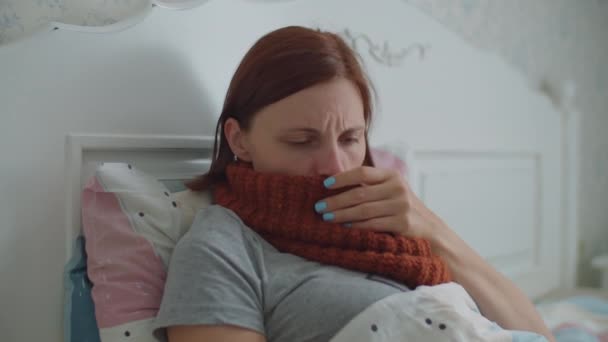Sick young woman laying in bed. Woman with warm scarf on neck coughs and blows her nose. Hand with pills appears. Virus disease treatment. — Stock Video