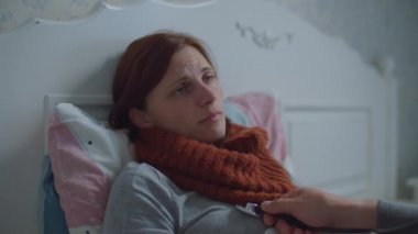 Hasta genç kadın yatakta yatıyor. Boynunda eşarp olan, öksüren ve burnunu silen bir kadın. Doktorlar steteskopla nefeslerini dinliyorlar..