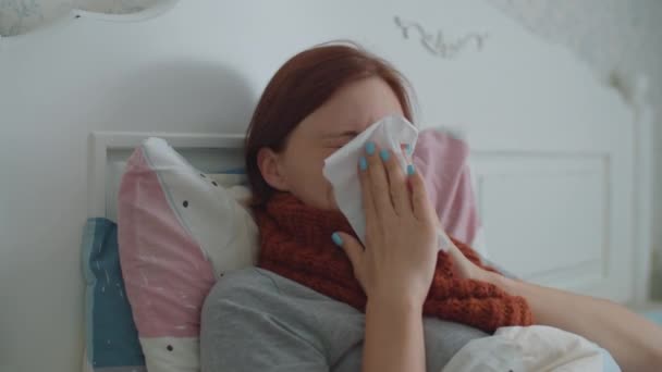 Jeune femme malade allongée dans son lit tenant une tasse de thé chaud avec du citron dans les mains. Femme avec écharpe chaude sur le cou tousse. Grippe et autres maladies respiratoires. — Video