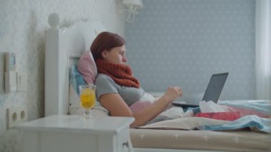 Evinden çalışan hasta bir genç kadın. Evraklar ve dizüstü bilgisayarla yatakta yatıyor. Öksürüğünde sıcak atkısı olan, burnunu silen ve belgelere bakan bir kadın. Evde grip ve diğer solunum hastalıkları.