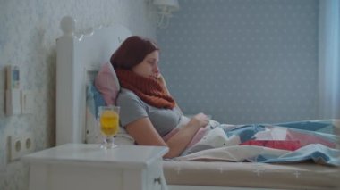 Hasta genç kadın yatakta uzanıyor ve cep telefonu çağrılarına cevap veriyor. Boynunda eşarp olan, öksüren ve burnunu silen bir kadın. Grip ve diğer solunum hastalıkları.