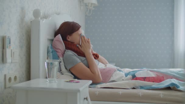 Une jeune femme malade tousse, se mouche et mesure sa température avec un thermomètre infrarouge électronique. La personne prend la pilule allongée dans son lit à la maison. Femme souffre d'une maladie virale saisonnière. — Video