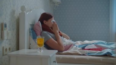 Hasta genç bir kadın elinde limonlu bir fincan sıcak çayla yatakta yatıyor. Boynunda eşarp olan, öksüren ve burnunu silen bir kadın. Grip ve diğer solunum hastalıkları.