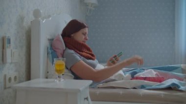 Hasta genç kadın yatakta uzanıyor ve cep telefonu çağrılarına cevap veriyor. Boynunda eşarp olan, öksüren ve burnunu silen bir kadın. Grip ve diğer solunum hastalıkları.