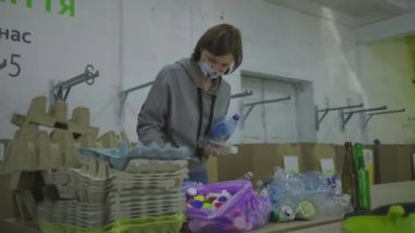 30 'lu yaşlardaki koruyucu maskeli genç bir kadın metal kutular, plastik ve cam şişeler gibi geri dönüşüm atıklarını sıralıyor. Çevreyi kurtarmak, plastik tüketimini azaltmak. Sıfır atık.