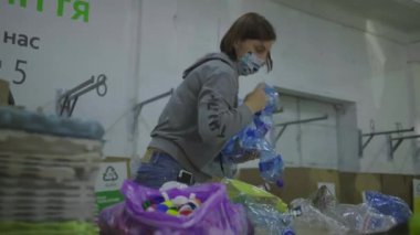 30 'lu yaşlardaki koruyucu maskeli genç bir kadın metal kutular, plastik ve cam şişeler gibi geri dönüşüm atıklarını sıralıyor. Çevreyi kurtarmak, plastik tüketimini azaltmak. Sıfır atık.