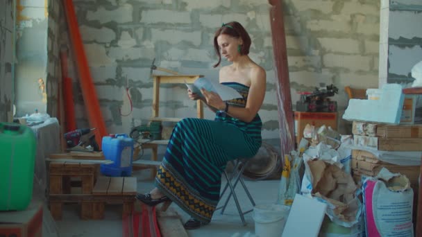 30 років жінка в одязі дивиться креслення ремонту будинку на будівельному майданчику. Власник жіночої квартири мріє про новий дизайн інтер'єру. Людина в новій квартирі . — стокове відео