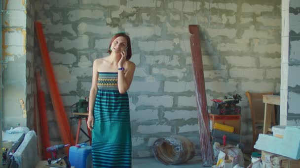 Mujer adulta joven hablando por teléfono móvil y caminando en el sitio de construcción. Mujer es feliz con la renovación del apartamento y habla con entusiasmo con su amigo. — Vídeos de Stock