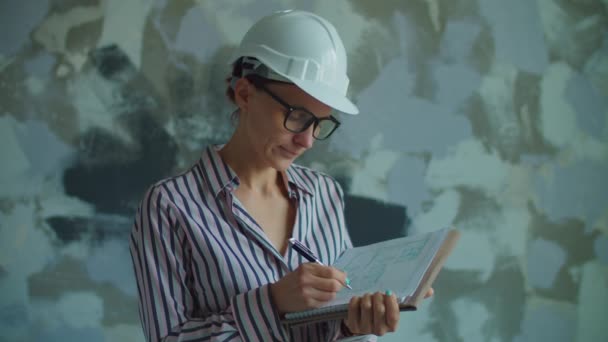 Junge Arbeiterinnen mit weißem Hut und Brille stehen mit Bauplänen in der Hand. Polier überprüft den Prozess der Haussanierung. Frau mit weißem Helm lächelt in die Kamera. — Stockvideo