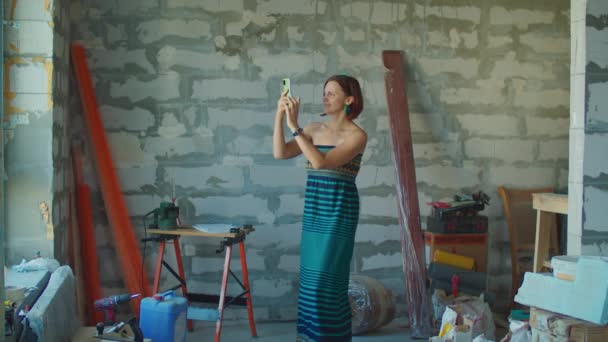 Žena v zelených šatech fotí renovaci domu na mobilu. Šťastná žena sní o interiérovém designu pro svůj nový byt. — Stock video