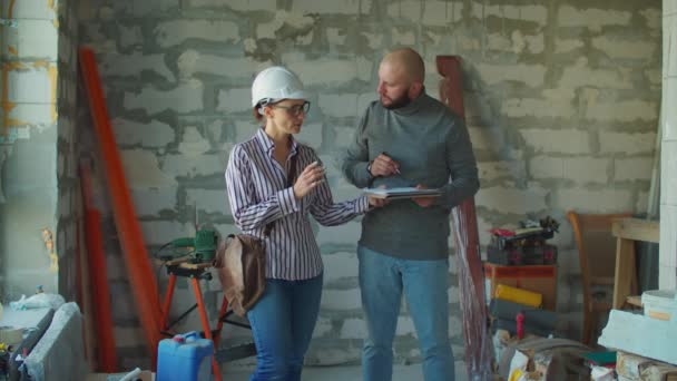 Joven barbudo firmando documentos para la capataz en un sombrero blanco. El hombre da dinero para la renovación de la casa en la obra. — Vídeos de Stock