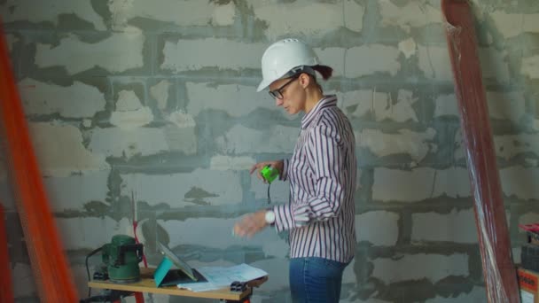 Jonge vrouwelijke voorman in witte hardhoed die werkt met tabletcomputer en papieren blauwdrukken. Vrouwelijke werknemer op de bouwplaats. — Stockvideo