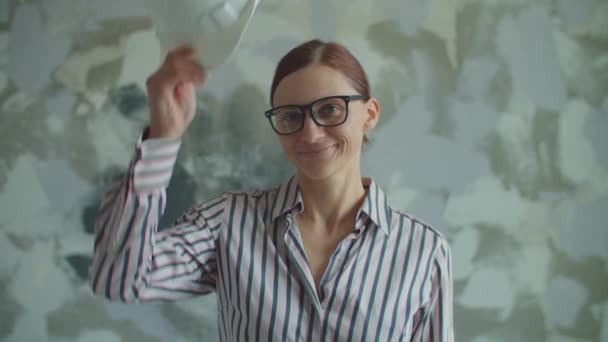 Молода 30 років жінка в окулярах одягає біле жорстко, дивлячись на камеру. Усміхнена жінка-лідерка задоволена ремонтом будинку . — стокове відео
