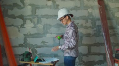 Beyaz şapkalı genç kadın ustabaşı tablet bilgisayar ve kağıt planlarla çalışıyor. İnşaat alanında çalışan kadın işçi..