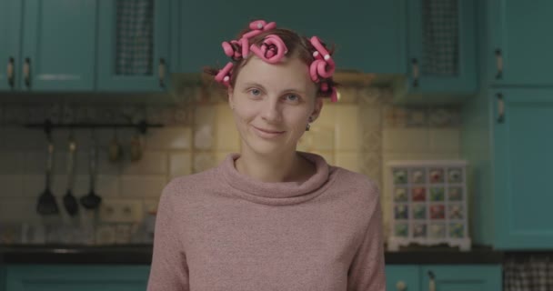 Ung rolig kvinna med rosa papiljotter på huvudet håller plattan med hemmagjorda eclairs och ler tittar på kameran. — Stockvideo