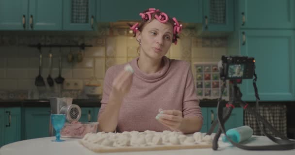 Γυναίκα blogger τροφίμων μαγείρεμα dumplings και καταγραφή βίντεο στην κάμερα. Χαμογελαστή νεαρή γυναίκα με μπούκλες μαλλιών που δείχνει το αποτέλεσμα της μαγειρικής της στους οπαδούς των μέσων κοινωνικής δικτύωσης. — Αρχείο Βίντεο