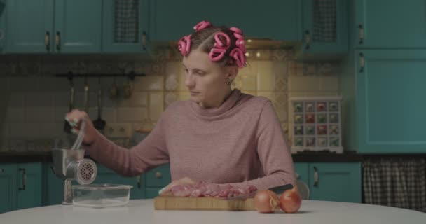 30 anos mulher jovem com encrespadores de cabelo na cabeça cozinhar carne em picador sentado na cozinha. dona de casa cozinhar em casa sozinho. — Vídeo de Stock